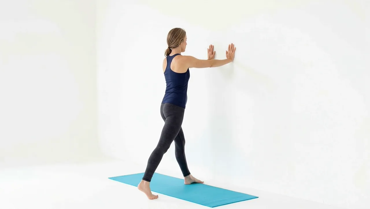Looping video demonstration of the Wall Calf Stretch exercise — a physician-designed movement performed on a mat in a bright studio.